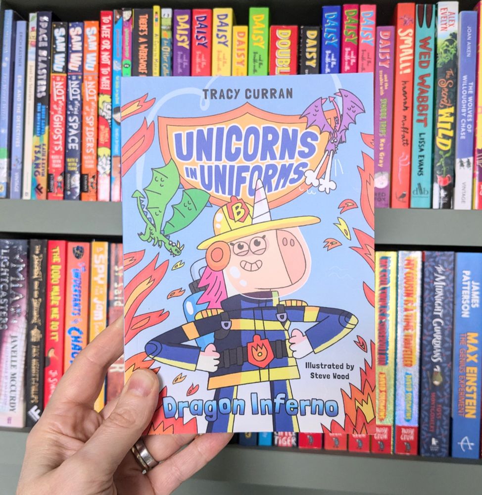 The cover of Unicorns in Uniforms in front of a colourful bookshelf. 