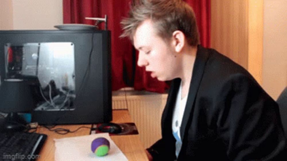 a man is sitting at a desk with a computer and a ball on it