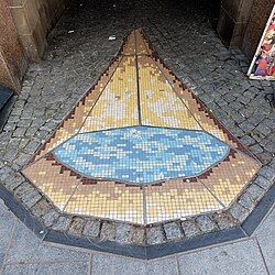 A large mosaic cone filled with water on the floor of a cobbled street. 