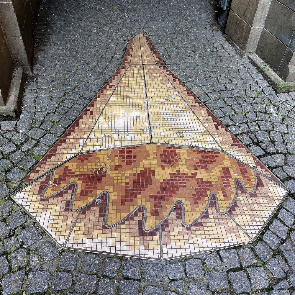 A large mosaic cone filled with flames on the floor of a cobbled street. 