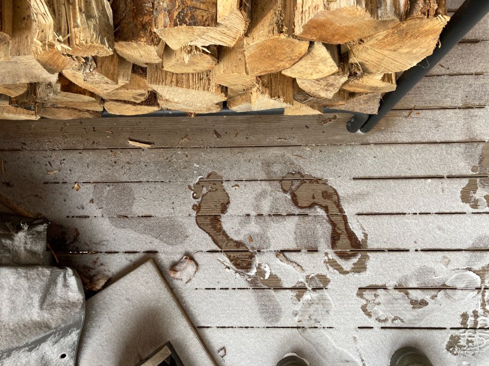 Snowy porch floor with barefoot prints next to a firewood pile.