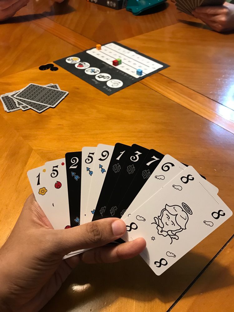 A hand of cards of Angels and Devils and a scoreboard is in the background