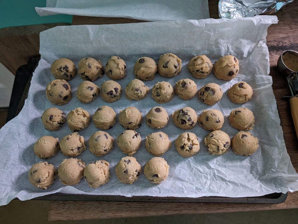 A baking sheet covered with parchment paper with lots of balls of cookie dough lined up on it.