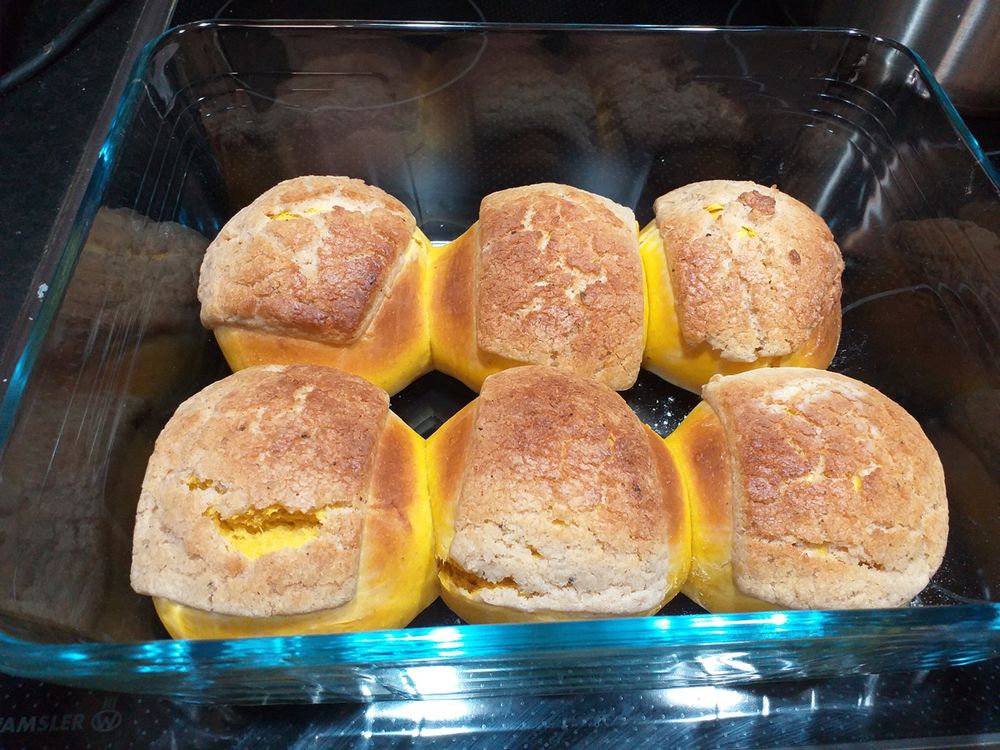 Six plump orange colored rolls topped with a spiced sugar crust in a pyrex/glass dish