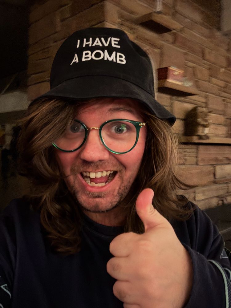 Pictured is Michael Kovach giving a thumbs up while wearing a cool hat with text that likely should not be typed out.