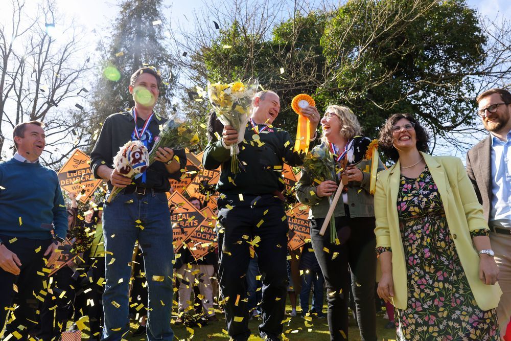 Ed Davey celebrates with Lib Dems amid confetti, flowers, and hobby horses.