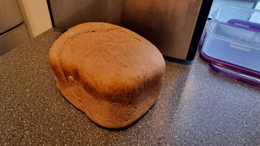 Ein selbstgemachtes Zimtbrot vor einem Brotbackautomaten. Beides befindet sich auf einer anthrazit-melierten Arbeitsfläche