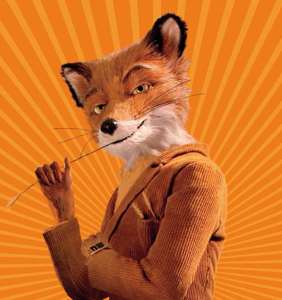 A stop-motion style anthropomorphic fox with orange fur and a sly expression stands in a confident pose. He wears a light brown corduroy suit and holds a piece of straw in his hand. The background is bright orange with radiating lines, adding to his charismatic and cheeky look.