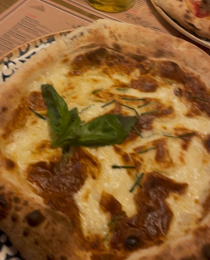 Eine Pizza mit geschmolzenem Käse und braun gebackenen Stellen, belegt mit frischem Basilikum.