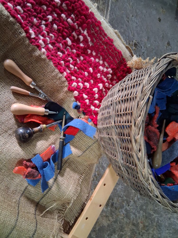 A photograph of a partly made rag rug, tools and loose rags.