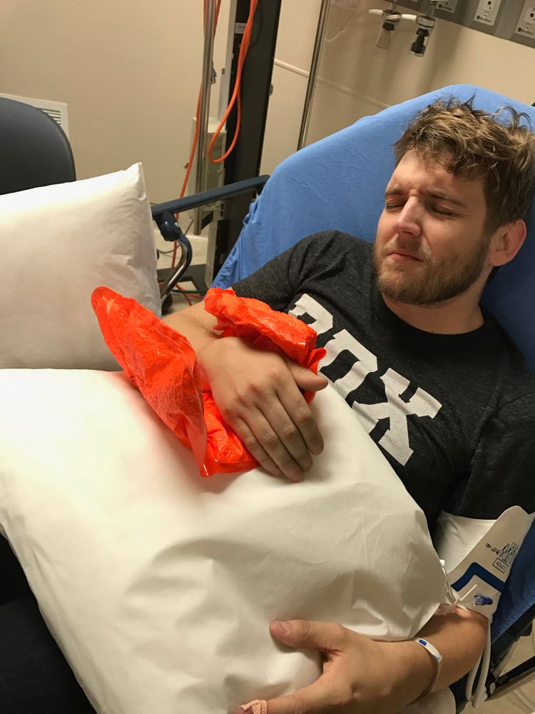 The same young man, grimacing in pain, his bayonet-fractured wrist held on a pillow in an inflatable temporary cast. Being wheeled to a waiting ambulance. Decidedly less excited. 