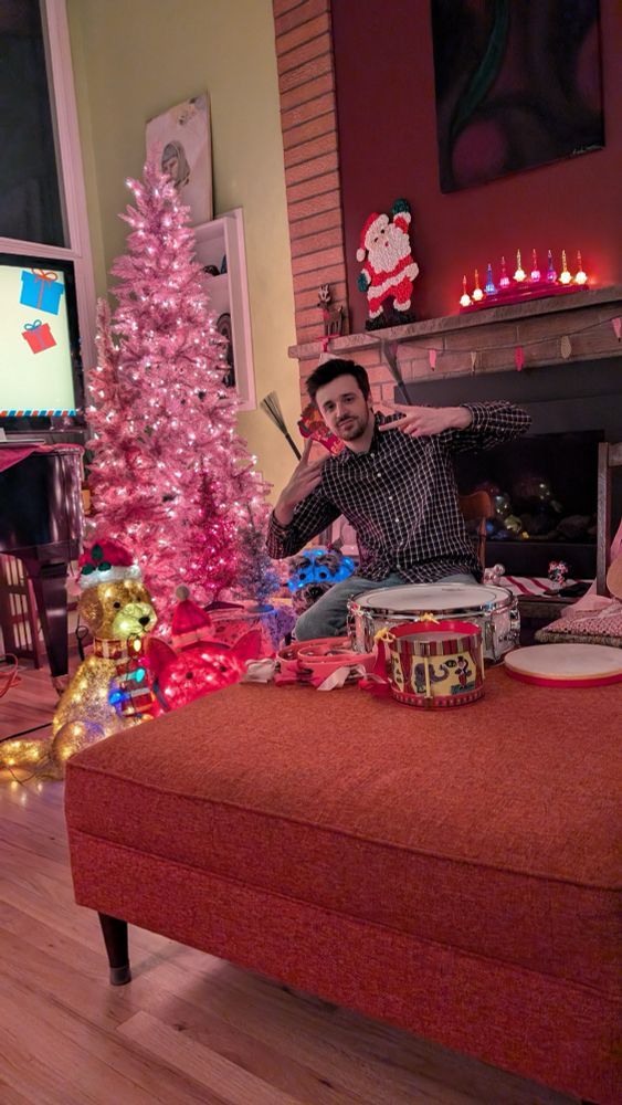 Alex at a Christmas-decorated house, holding drum brushes, making peace signs