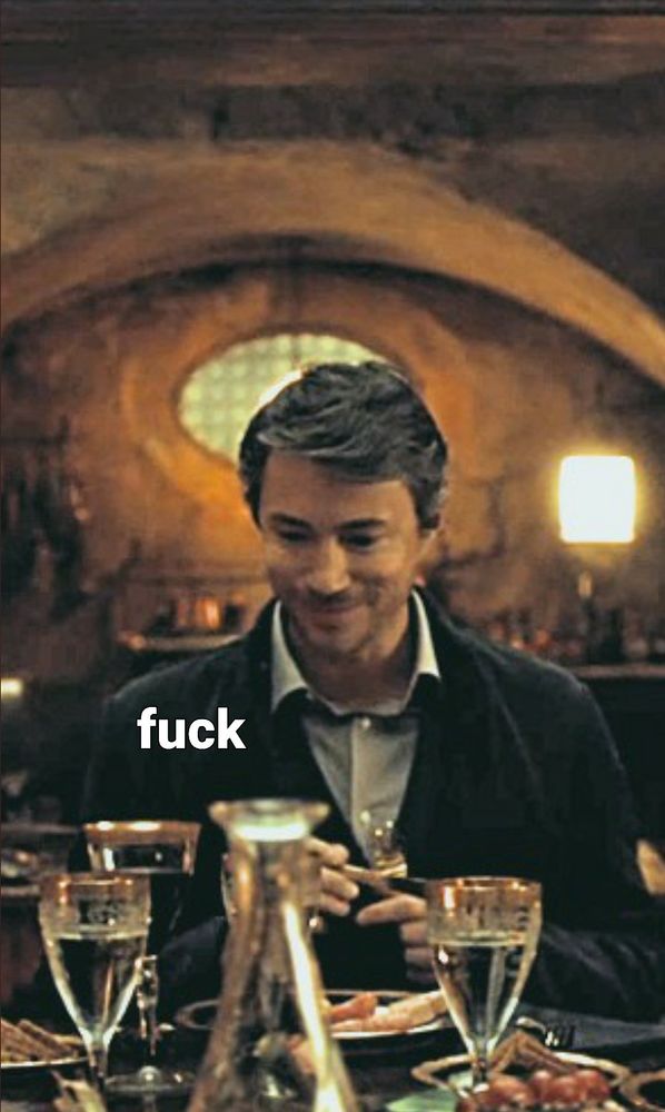 Anthony dimmond from Hannibal sat at a dinner table looking down awkwardly with the caption fuck in white text. He is a white man in his 30s with brown hair and stubble, wearing a dark suit jacket and a light grey collared shirt