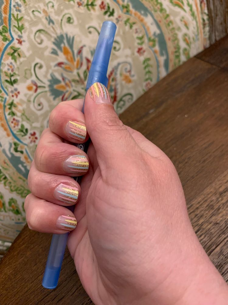 Close up of nails decorated with pink, gold, yellow, and blue ribbons
