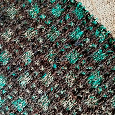patterned knitting of turquoise squares alternating with four dots, all on a chocolate brown background