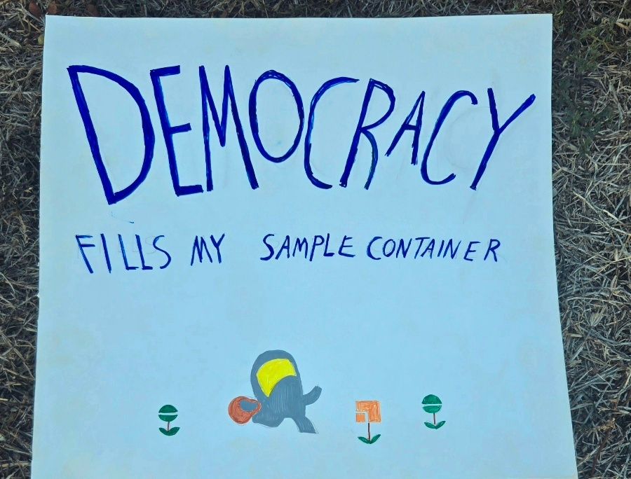 A sign made of poster board. It says "democracy fills my sample container."