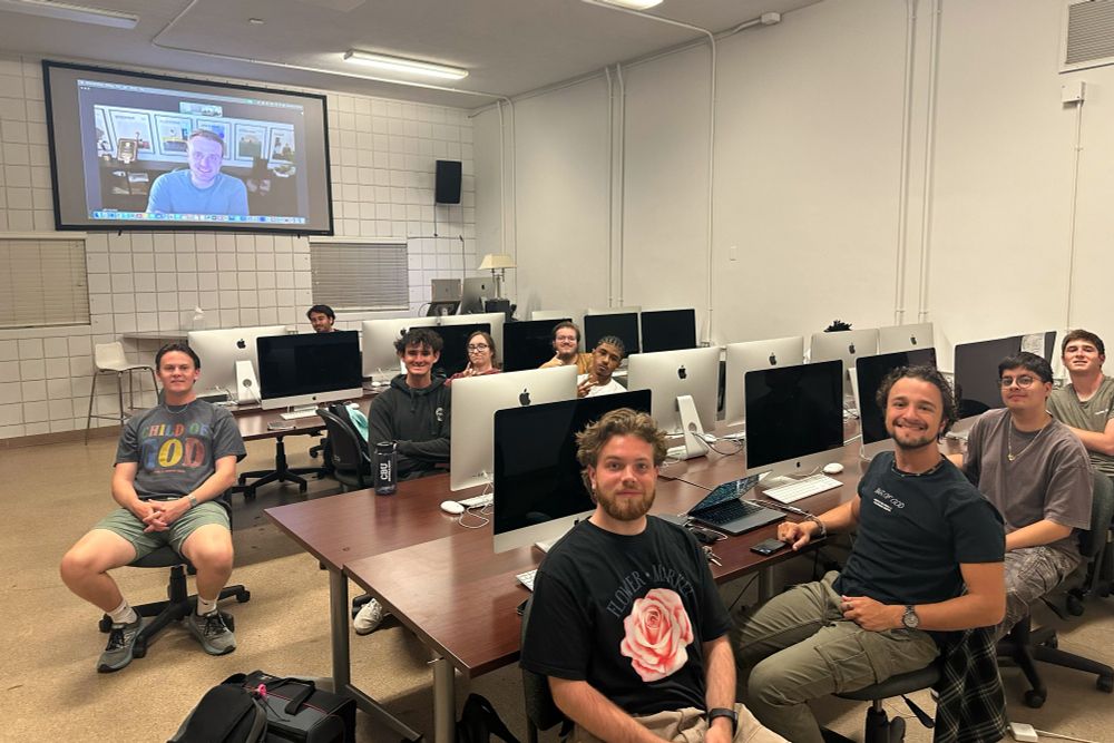 A computer lab classroom full of students posing for a picture with Corey Frost, who is projected on the screen above them.