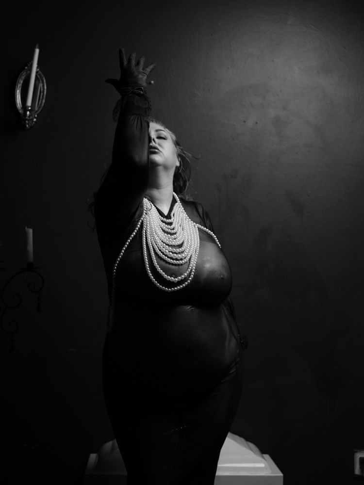 Model in wet dress, lace gloves, and pearl body jewelry. Face looking up, arm reaching up with hand open and palm facing away from the camera.