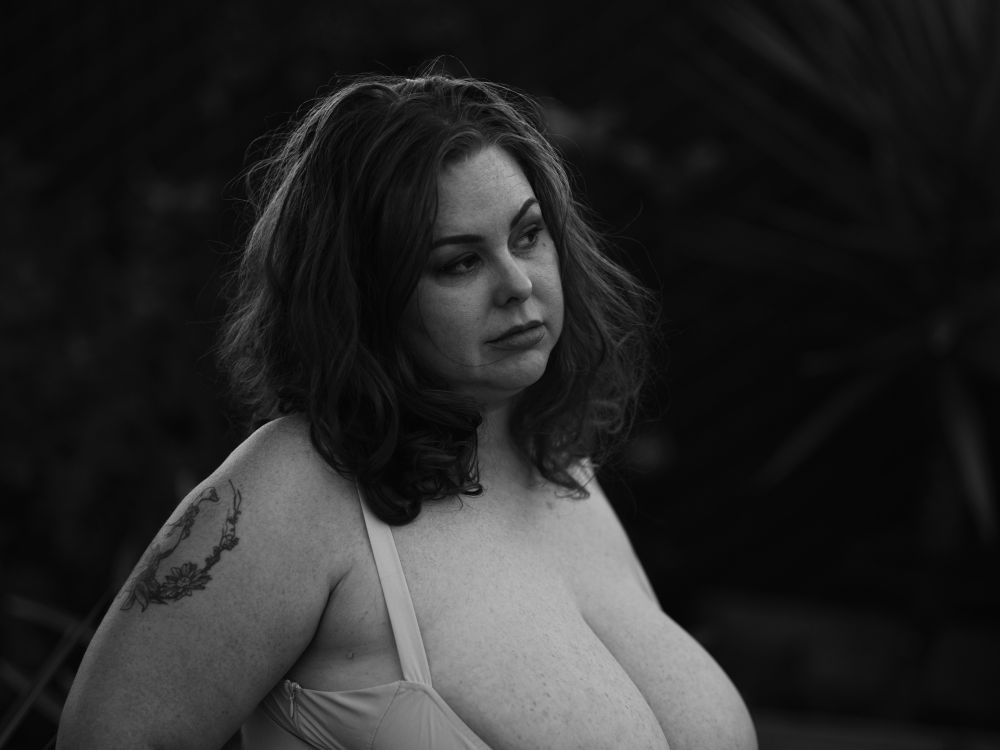 Model in low cut dress, looking to camera right. Black and white film simulation.