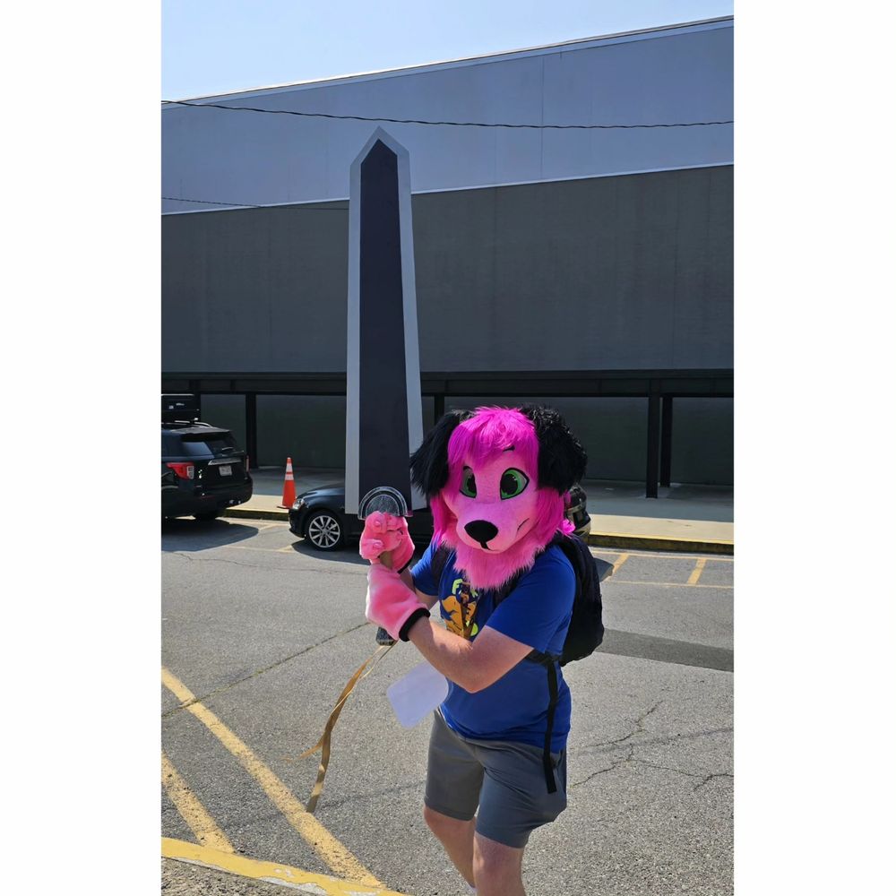 A pink doggy fursuiter named Billy raises his mighty sword and prepares to charge the camera