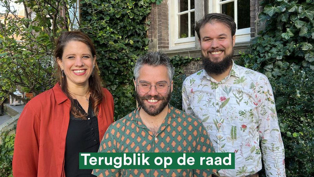 Van links naar rechts raadsleden ‘Leonie Gerritsen, Robin Smit en Jan Willem van den Bos van Partij voor de Dieren Den Haag. Ze staan lachend op de foto met Robin iets voor de andere twee. Achter hen groeien groene planten aan een muur.