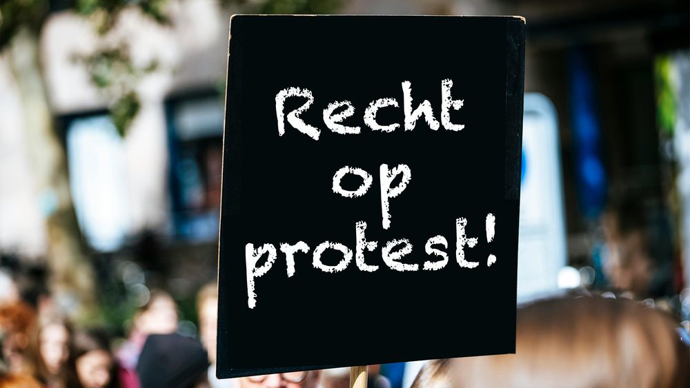 Een ge-edit zwart bord met witte tekst erop aanwezig bij een demonstratie. De tekst zegt Recht op protest!