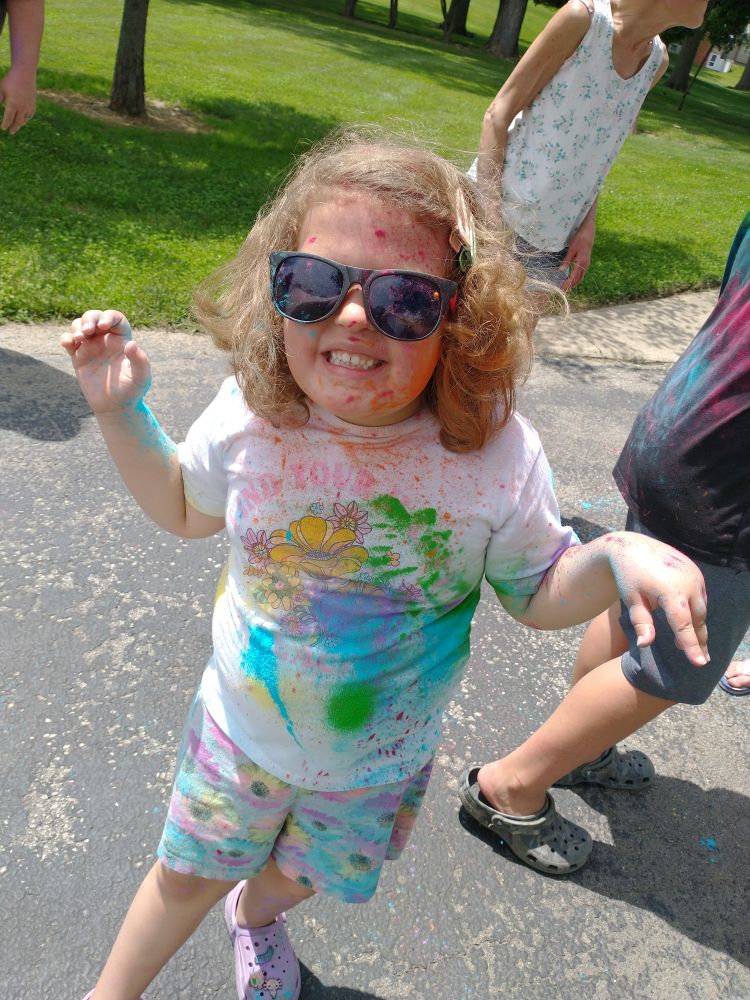 A little girl growling at the camera while covered in colored powder. 