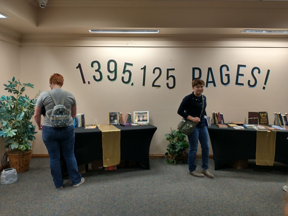 People browsing a table full of books. A sign on the wall says 1,395,125 pages. 