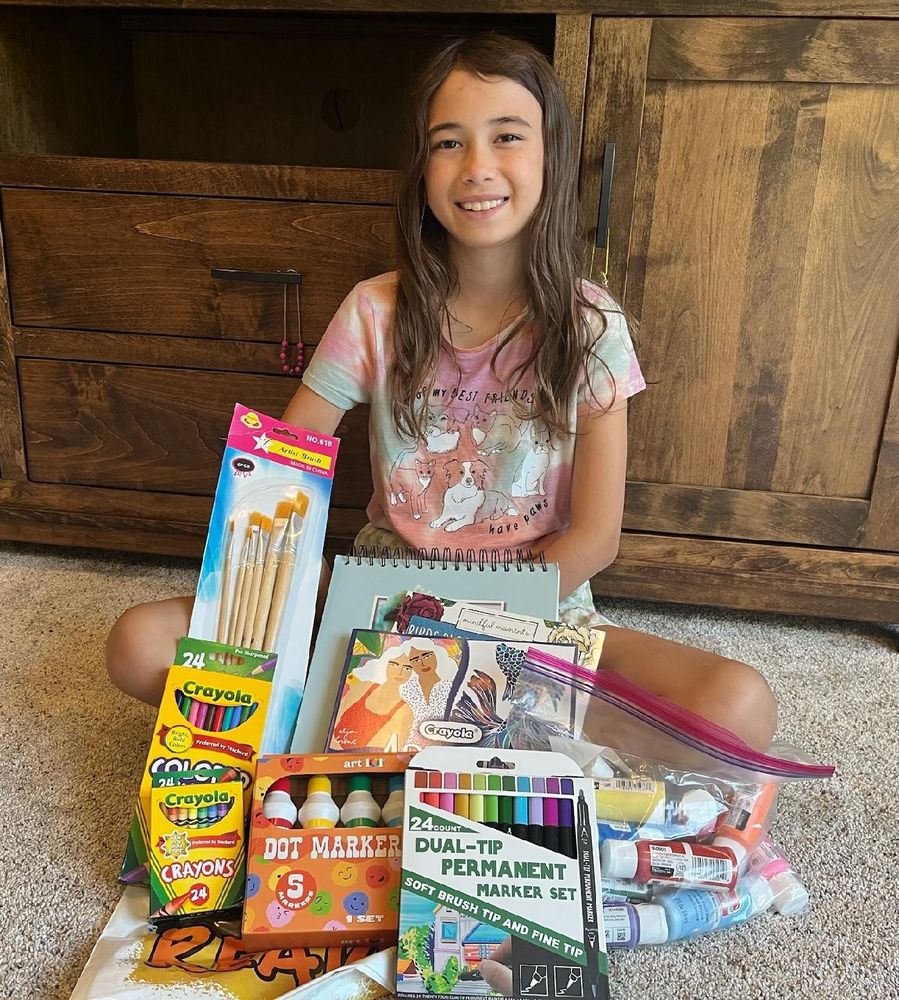 A young girl sitting on the floor surrounded by art supplies. 