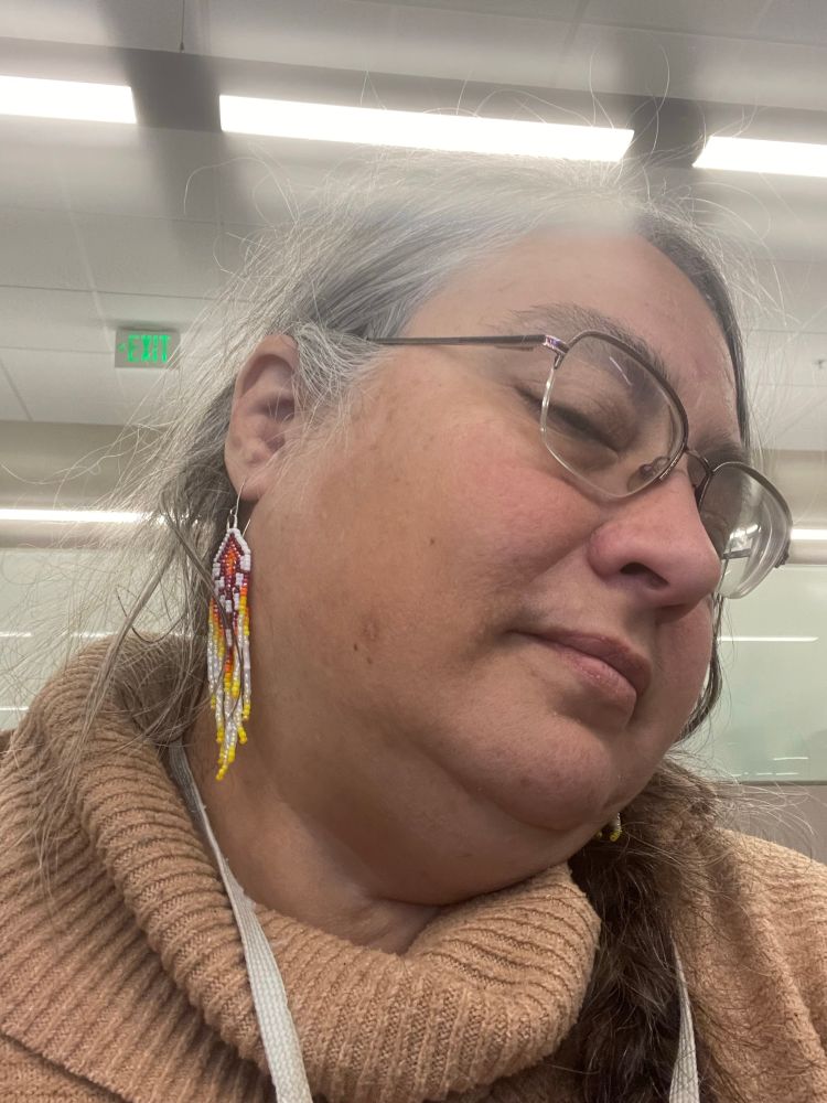 Beaded earrings in a red, orange, yellow, and white pattern worn by a middle-aged office worker with a beige turtleneck sweater