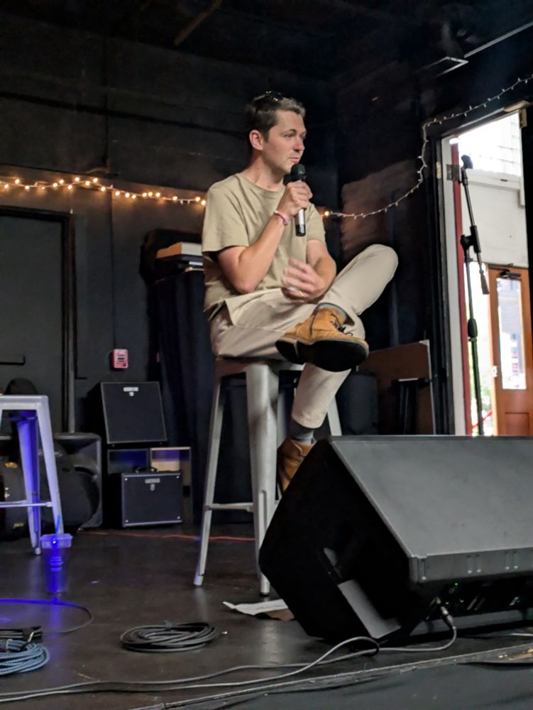 Singer Damian McGinty sitting on a stool holding a microphone.