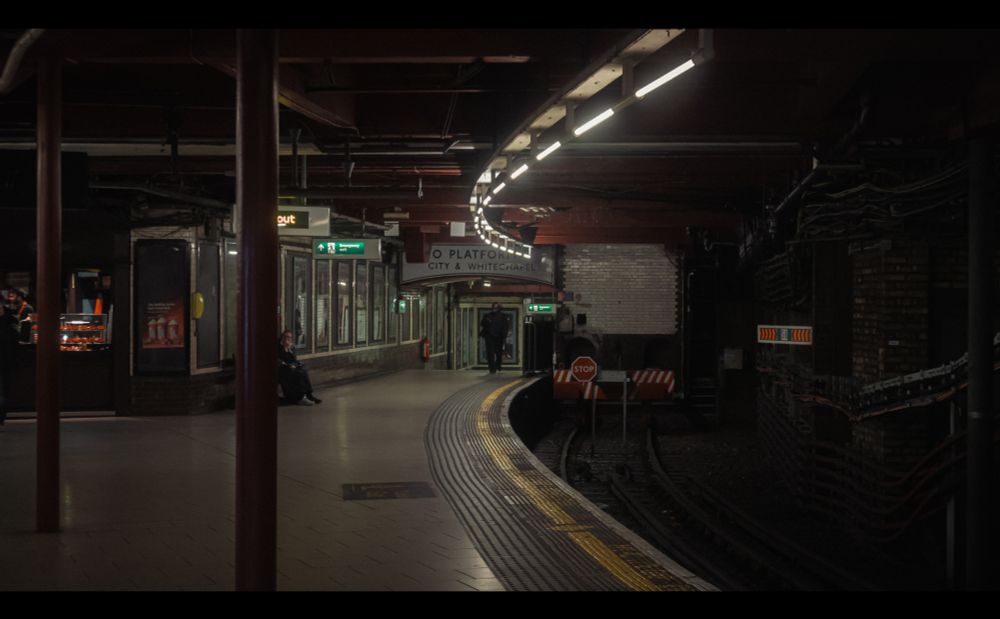 A dark tube station platform with a small amount of people