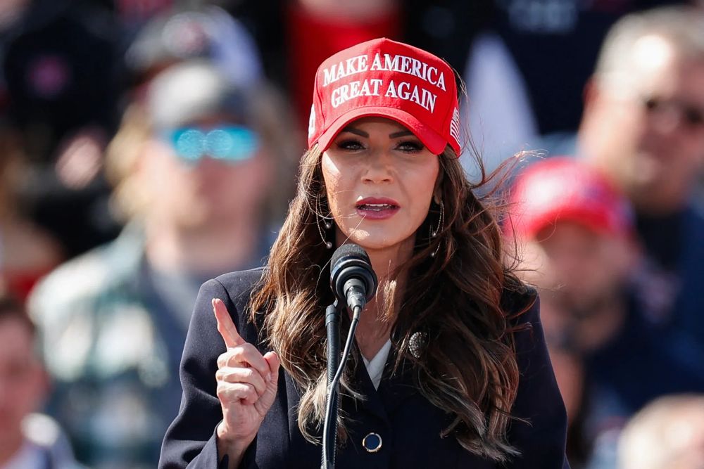 Kristi Noem, atual secretária de segurança interna dos EUA, discursa com boné vermelho do MAGA