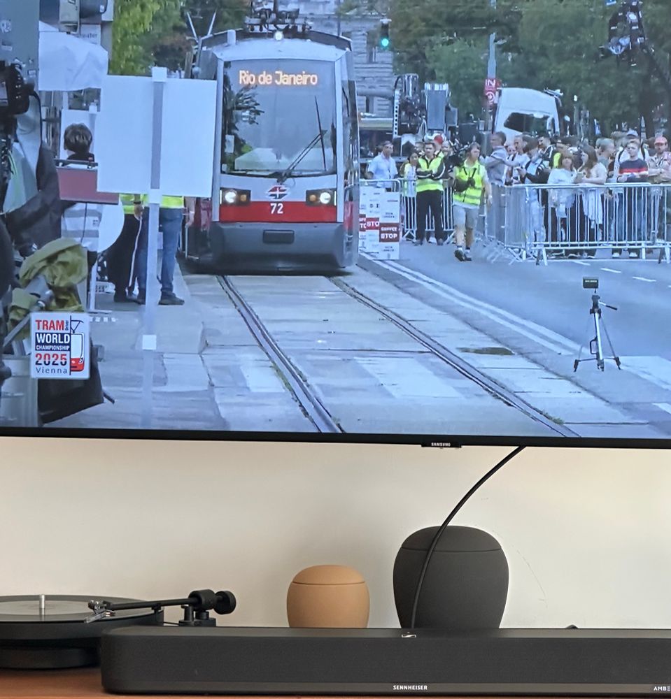 Imagem de um bonde com um letreiro luminoso com o destino "Rio de janeiro". Ao lado, público acompanha a competição. 