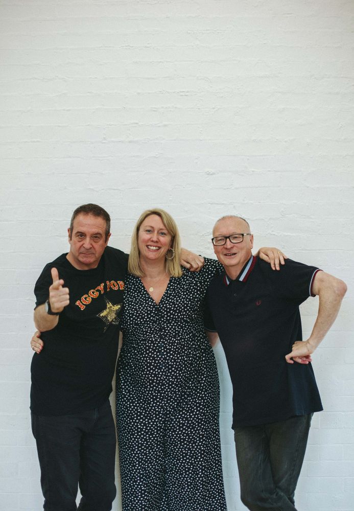Mark Thomas, Charlotte Bennett and Ed Edwards, posing with a white background. Mark points at the camera.