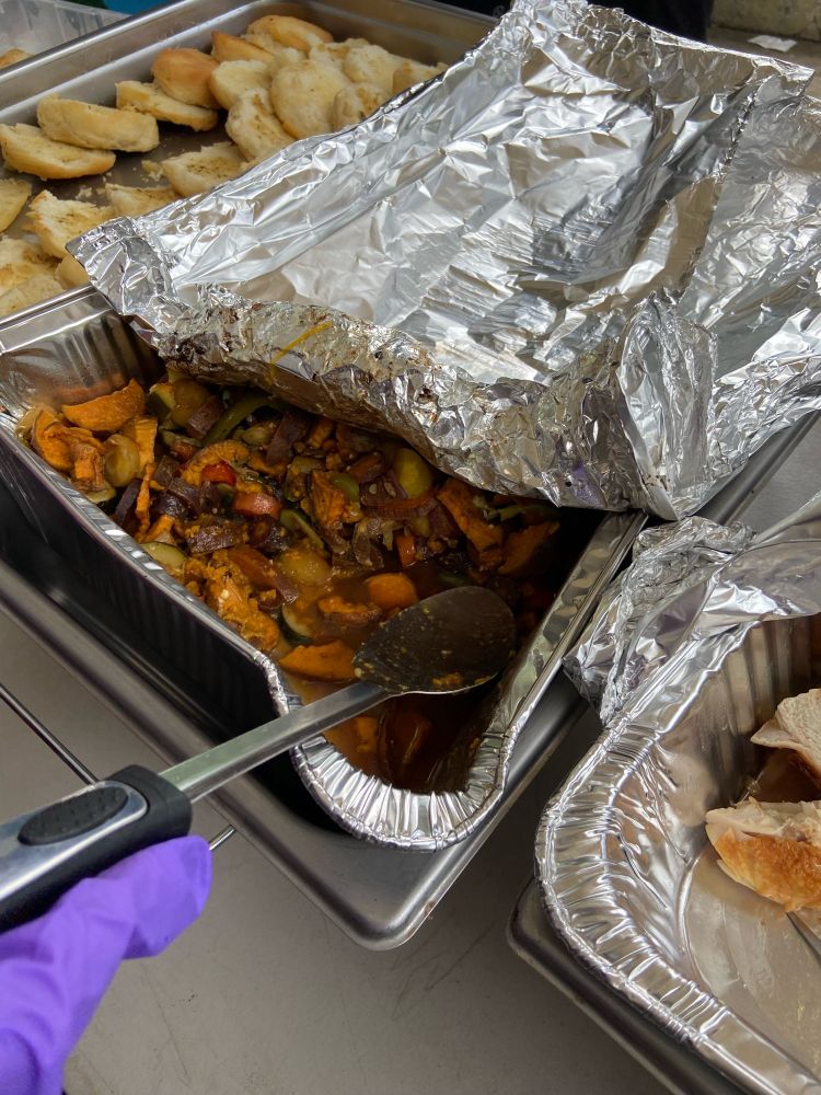 tray of mixed vegetables with a gloved hand holding a serving utensil