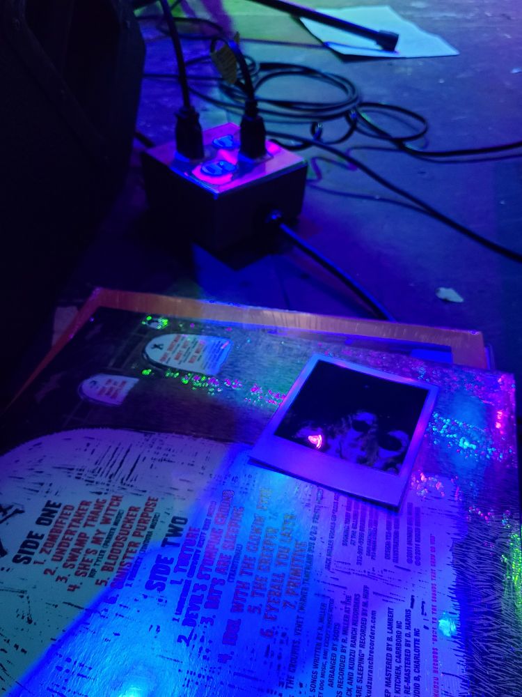 A close up of a vinyl and a Polaroid photo on a dark stage in a music venue