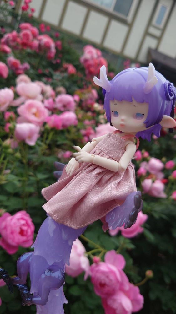 上半身が紫色の髪のぽんやりした女の子、下半身が透明感のある紫色の龍のドール、ずぃちゃんと、満開のピンクのばらたち