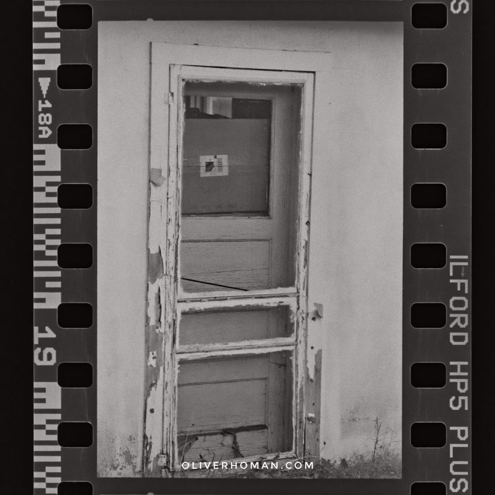 An old unused door with white paint peeling off. A large cardboard box is behind a second door. The stucco on the building is starting to come off.