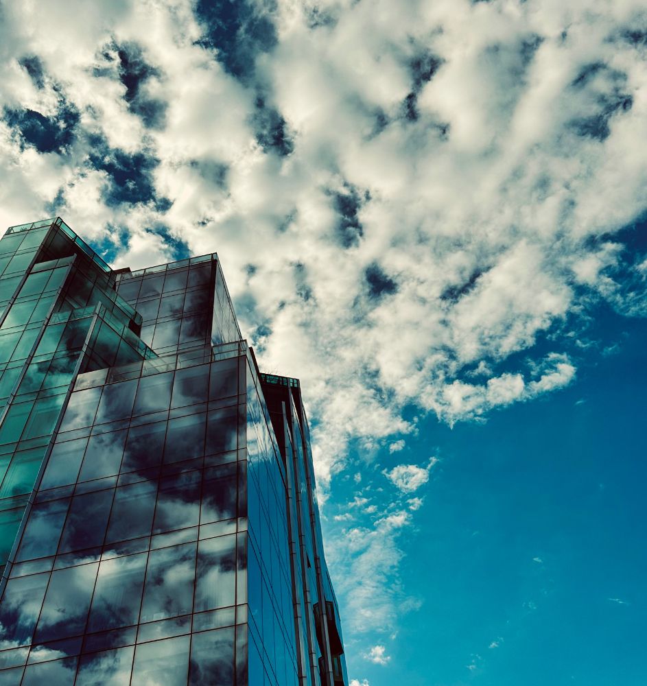 Left side of photo is a building with clouds reflecting off of it and right side is a blue sky with clouds.