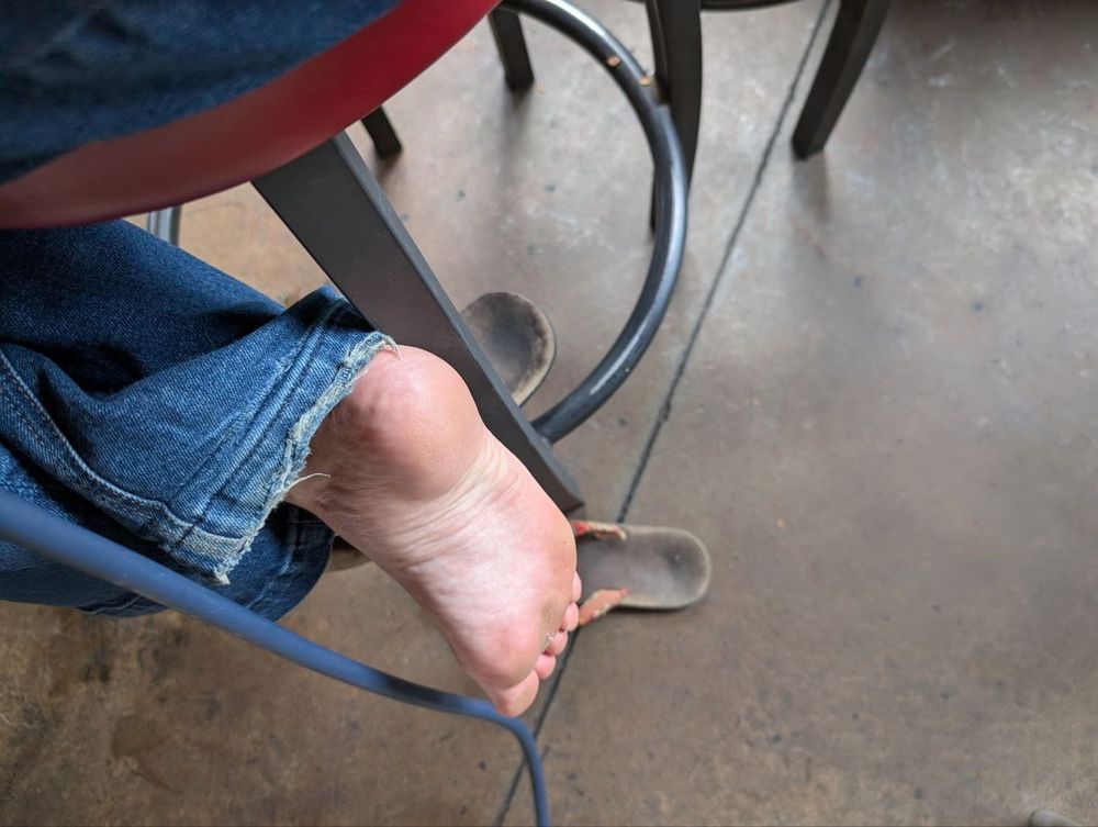 The bottom of a naked foot beneath under a bar stool.