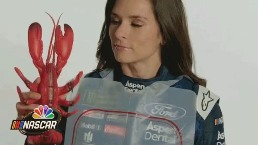 a woman is holding a lobster in front of a nascar sign