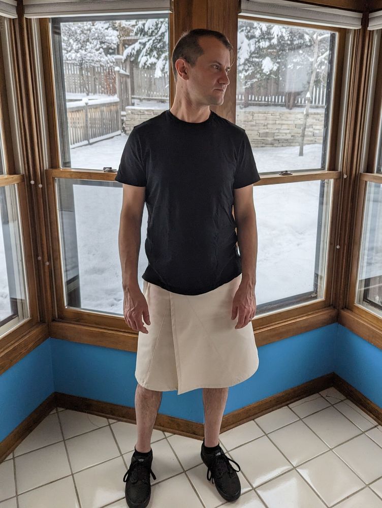 Man wearing a cream colored, knee-length wrap skirt with pockets