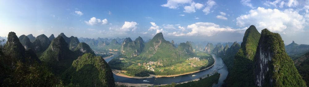 A view of the pointed green karst mountains surrounding the horseshoe bend of the LiJiang River, with blue sky sporting fluffy white clouds, near Yangshuo, China.