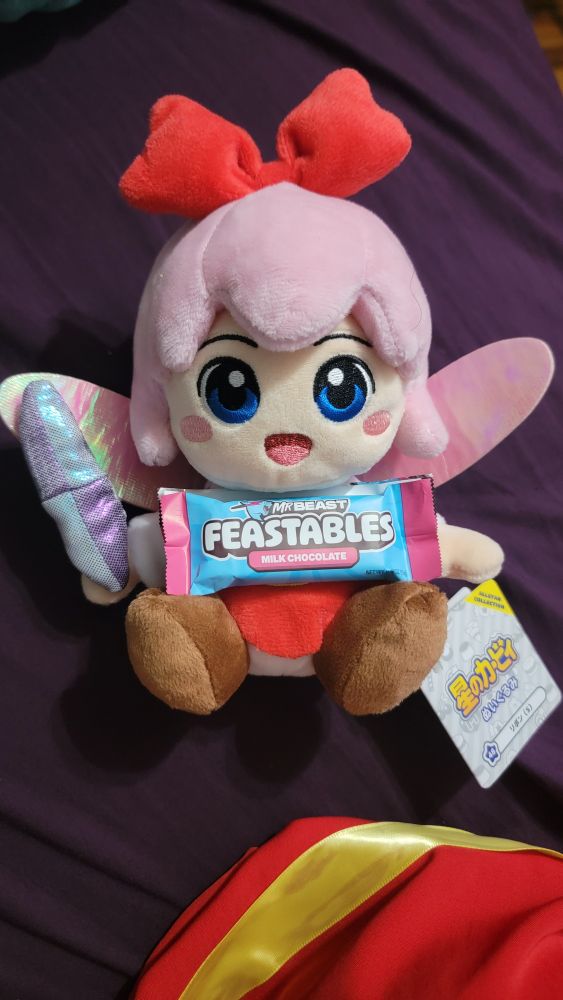 A plushie of ribbon from Kirby 64 The Crystal Shards holding a small Mr. Beast Feastables candy/chocolte bar
she will die eating this