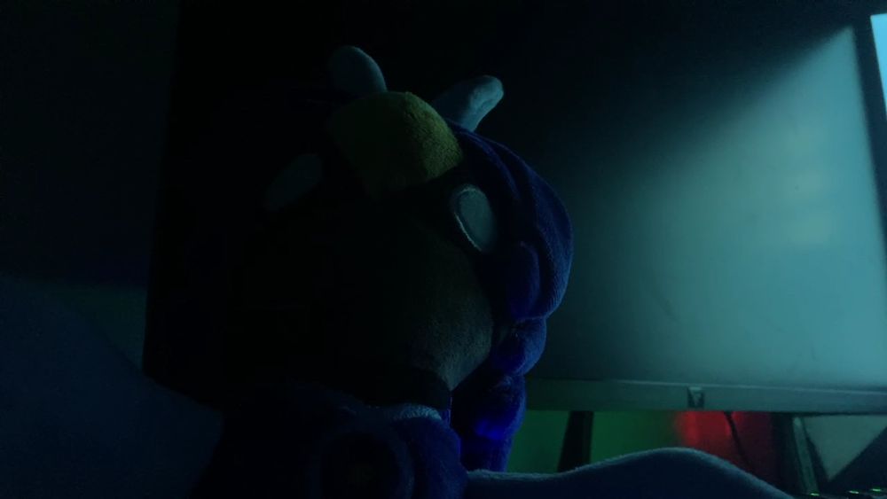 Alula plush, sitting menacingly in front of a bootlooping computer.