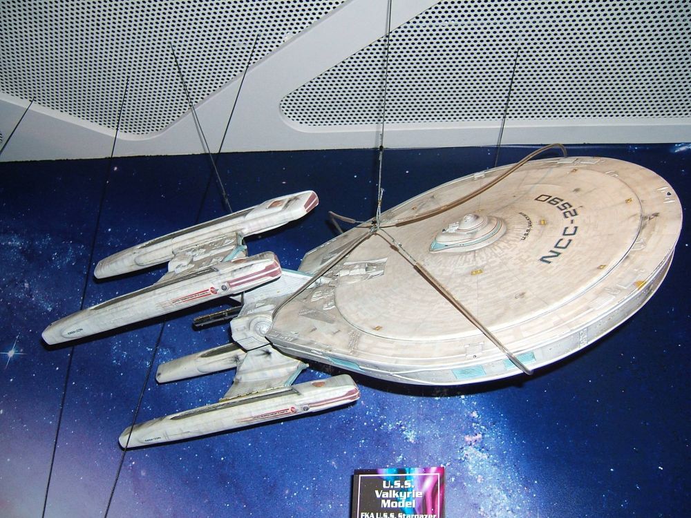 Studio model of a Constellation class ship from Star Trek. Its hanging from wires wrapped around it. On display at an exhibition.
