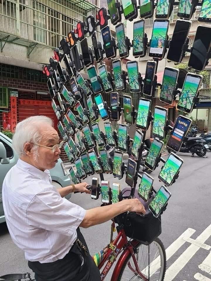 An older guy riding a bike with dozens of phones running Pokemon GO mounted on the handlebars