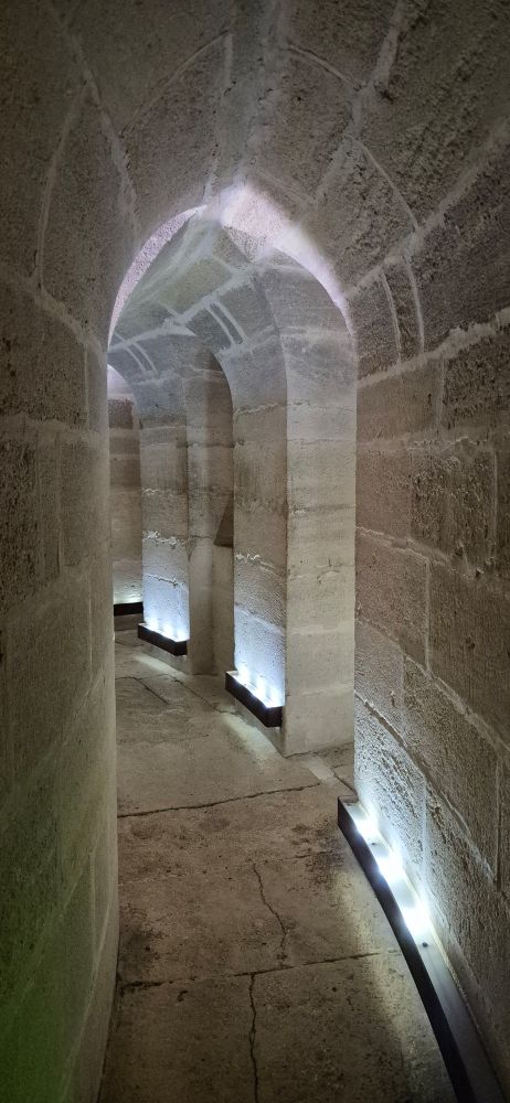Aif dem Bild sieht man einen Gang, der sich nach links im Inneren des Turms entkam der Außenwände windet. In Bodennähe ist dezentes Licgt angebracht. 
Die Wände bestehen aus großen, grauen Steinblöcken, die Bögen an der Decke laufen spitz zu und an der Außenwand sind sie alle paar Meter durch Nischen unterbrochen. 
Der Boden besteht aus großen Steinplatten. 
