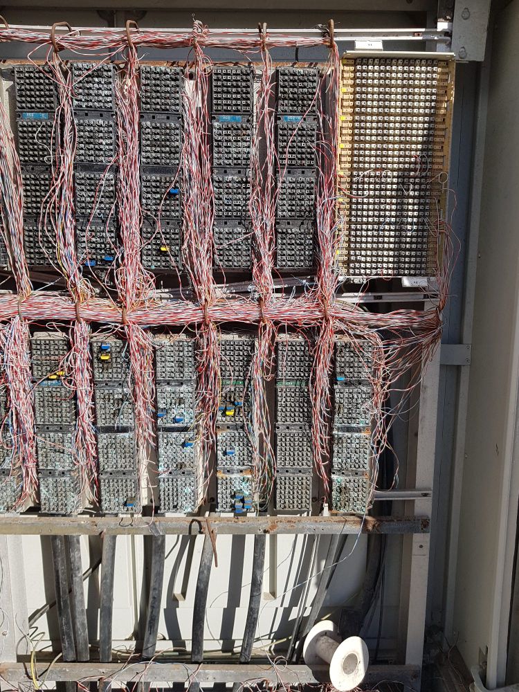 Man sieht einen offen stehenden Kasten ähnlich einem Sicherungskasten. Darin sind sehr viele rote Kabel und Stecker, die nach keinem erkennbaren Muster zusammengebaut sind. 